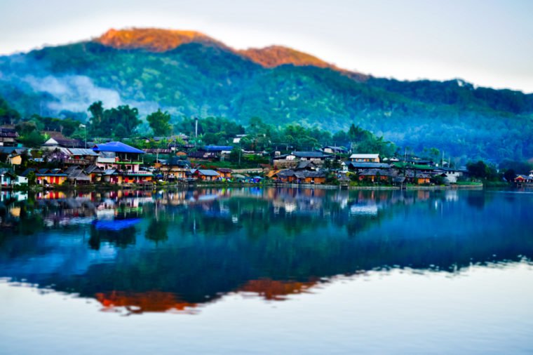 The village next to the river. The backdrop has mountains and beautiful blue turquoise sky. The river has a beautiful reflection. Village in Pai, Mae Hong Son, Thailand